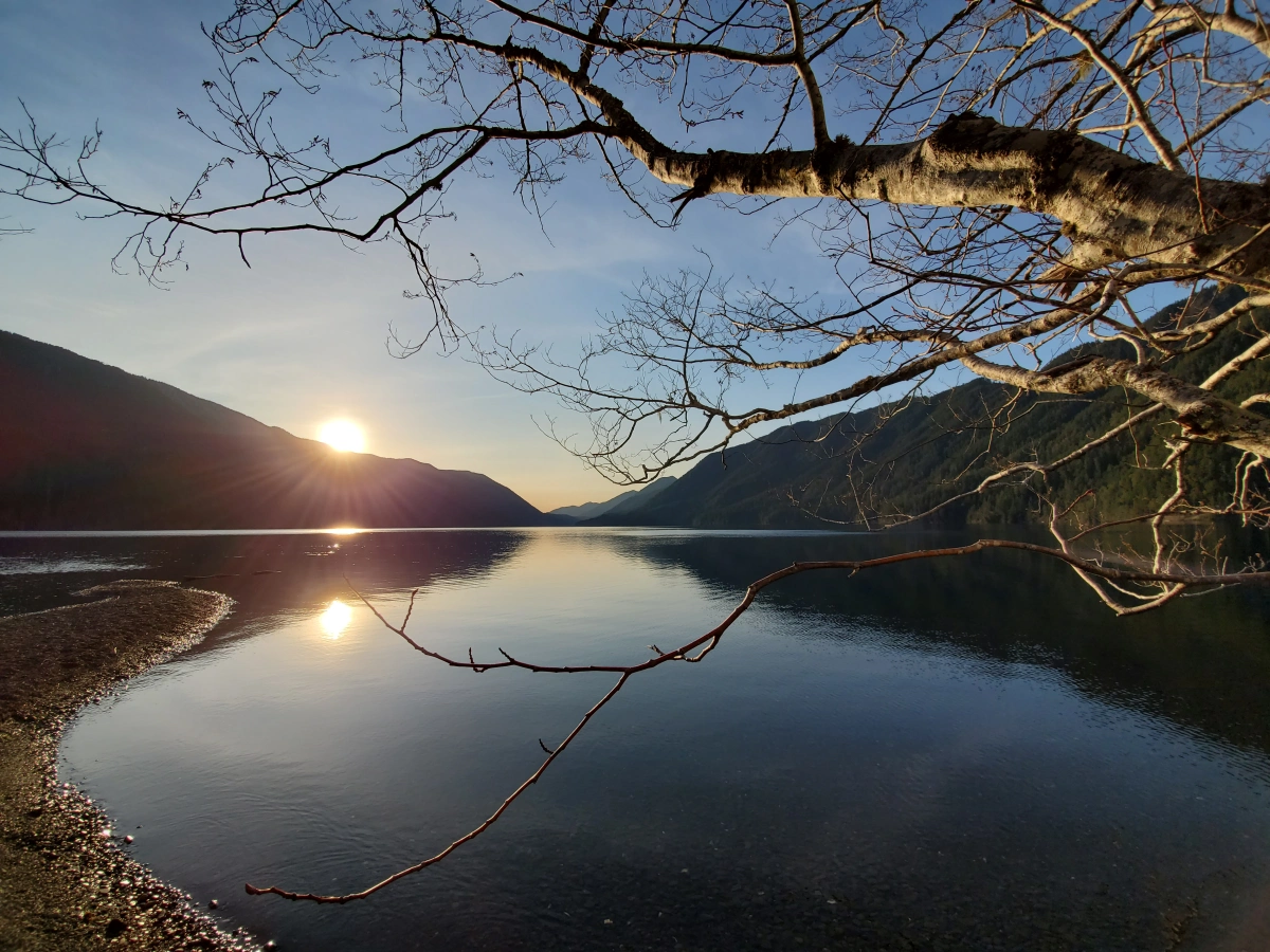 Sun setting behind a mountain by a lake.